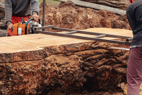 Craftsman using a chainsaw to cut a large live edge wood slab, highlighting the woodworking process.